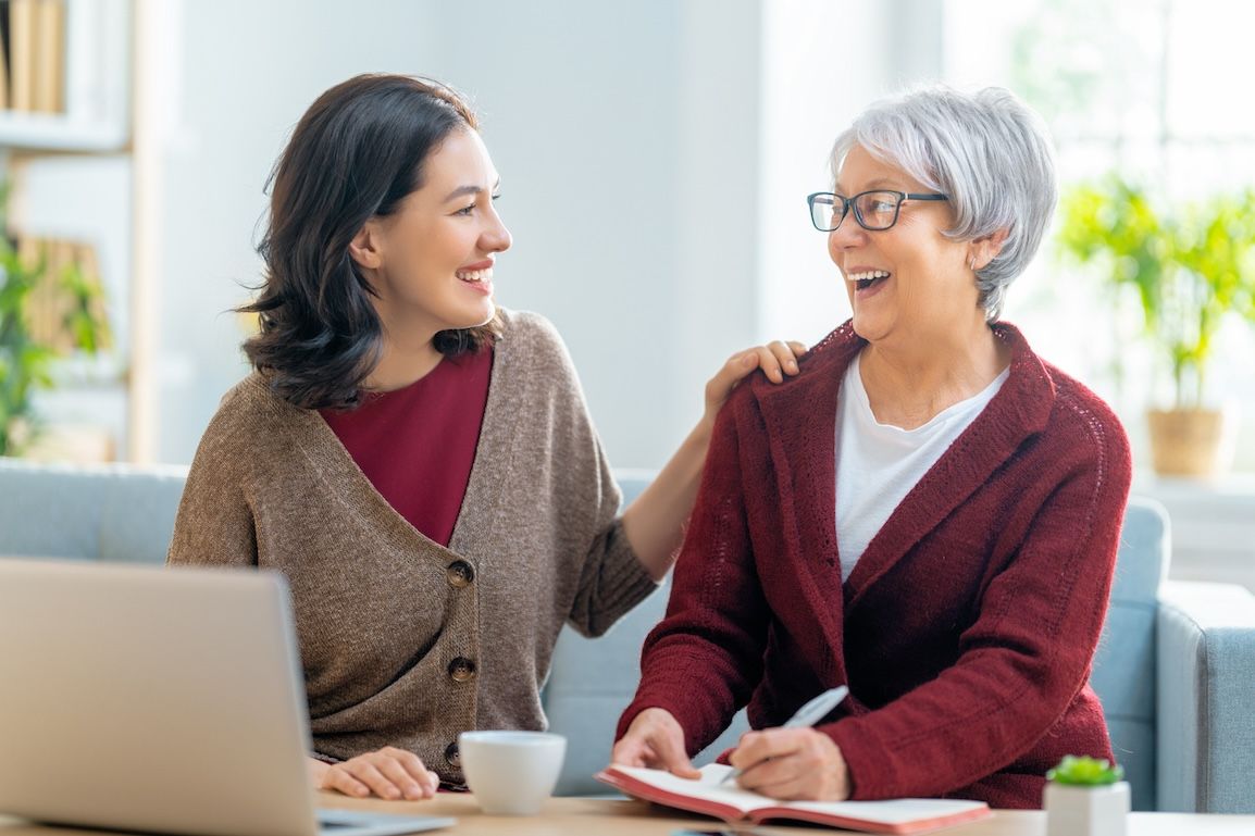 Supporting aging parents: adult daughter and senior mother smiling and talking at home.
