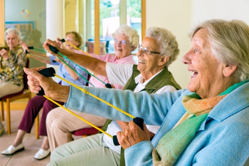 Senior adults smiling while exercising in a wellness class at a senior living community.