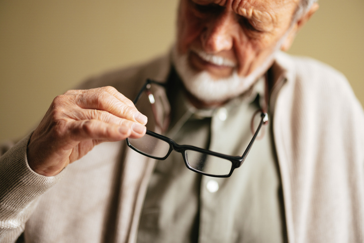 Transitioning from Independent Living to Assisted Living. Image is of an older man looking at his glasses.