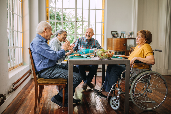 four seniors laughing, eating, and playing a game at senior living community
