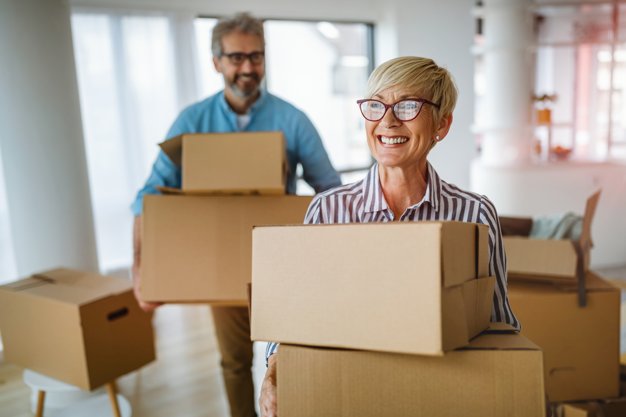 Senior adult man and woman holding boxes. Moving into their new apartment.