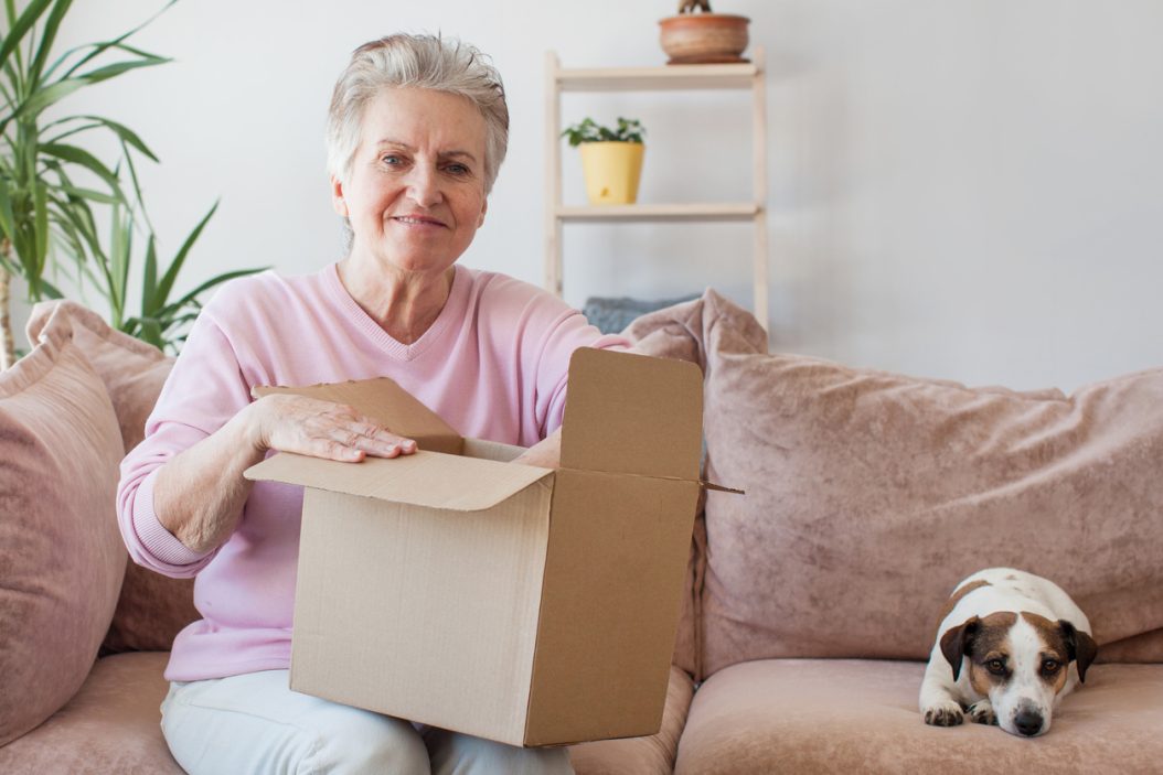 Senior adult woman unpacking in her new apartment with her dog nearby, settling into pet-friendly senior living.