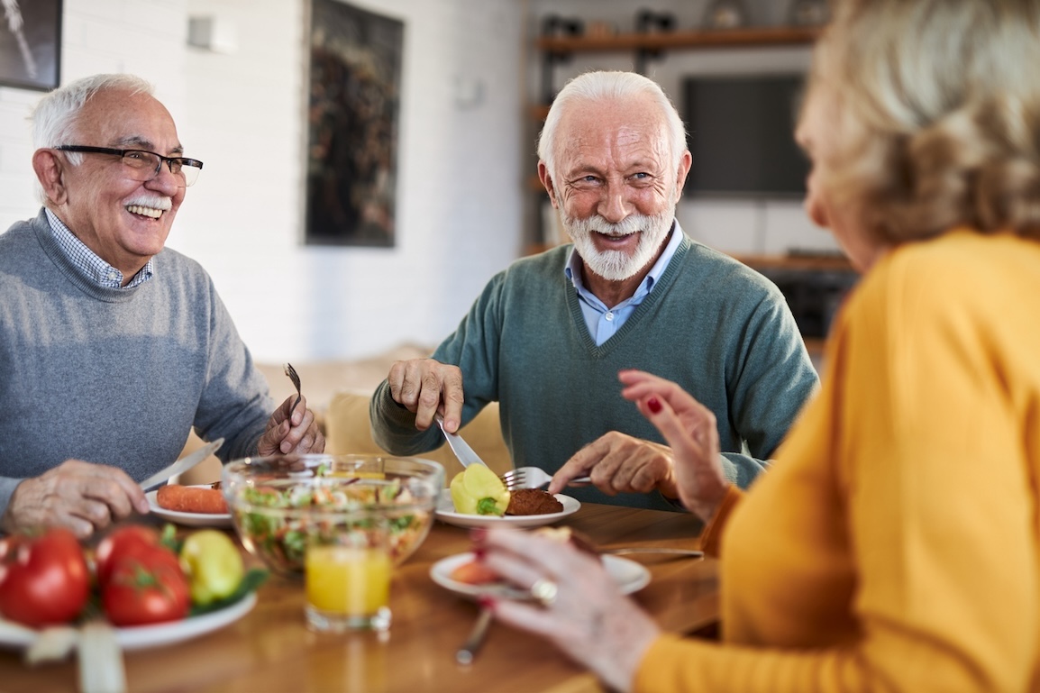 Group of happy senior adults enjoying a meal together in a retirement community dining area, laughing and talking.