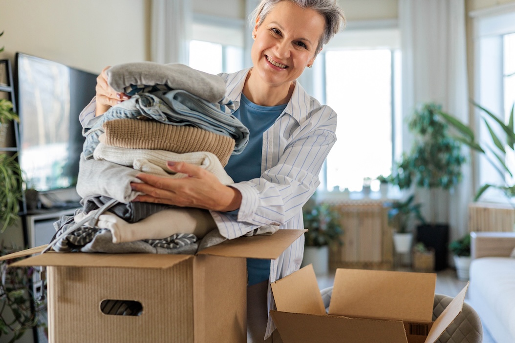 Smiling senior woman organizing clothing into a box in her apartment.