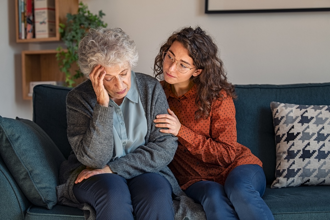 Young woman comforting senior adult on couch, offering support for memory concerns
