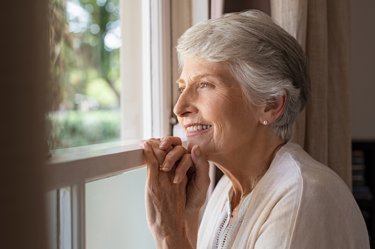 Senior adult smiling and reflecting by window in a calm home setting